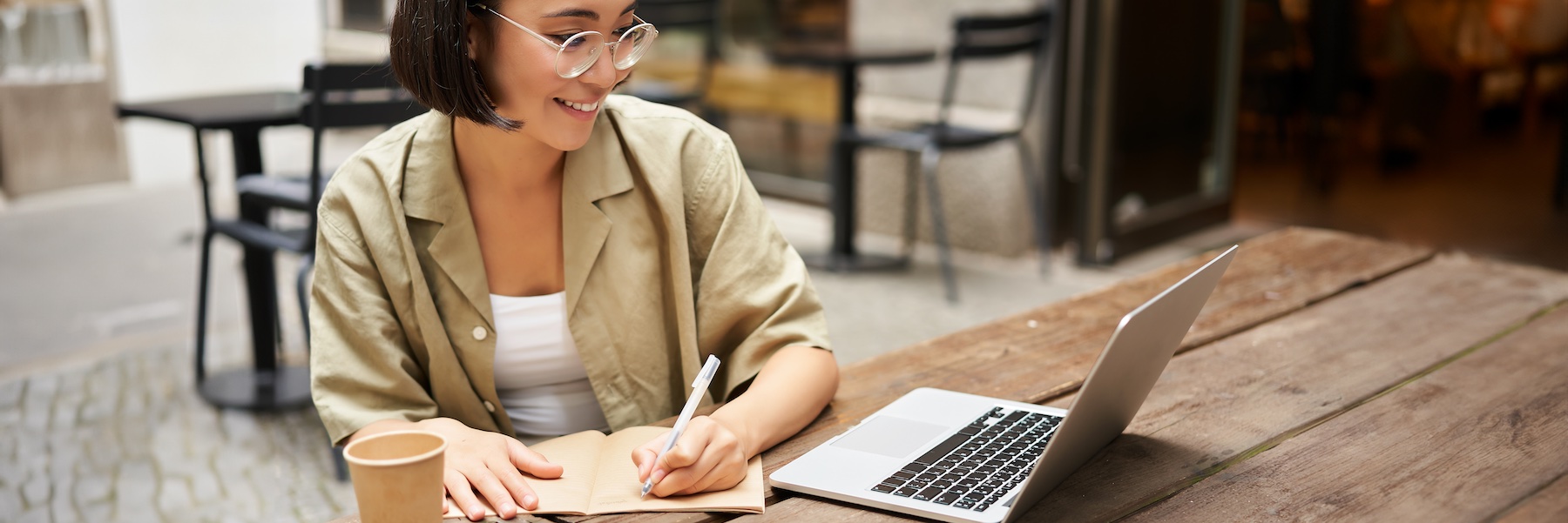 Smiling woman using a laptop and writing in a notebook, representing active patient engagement in thyroid health management.